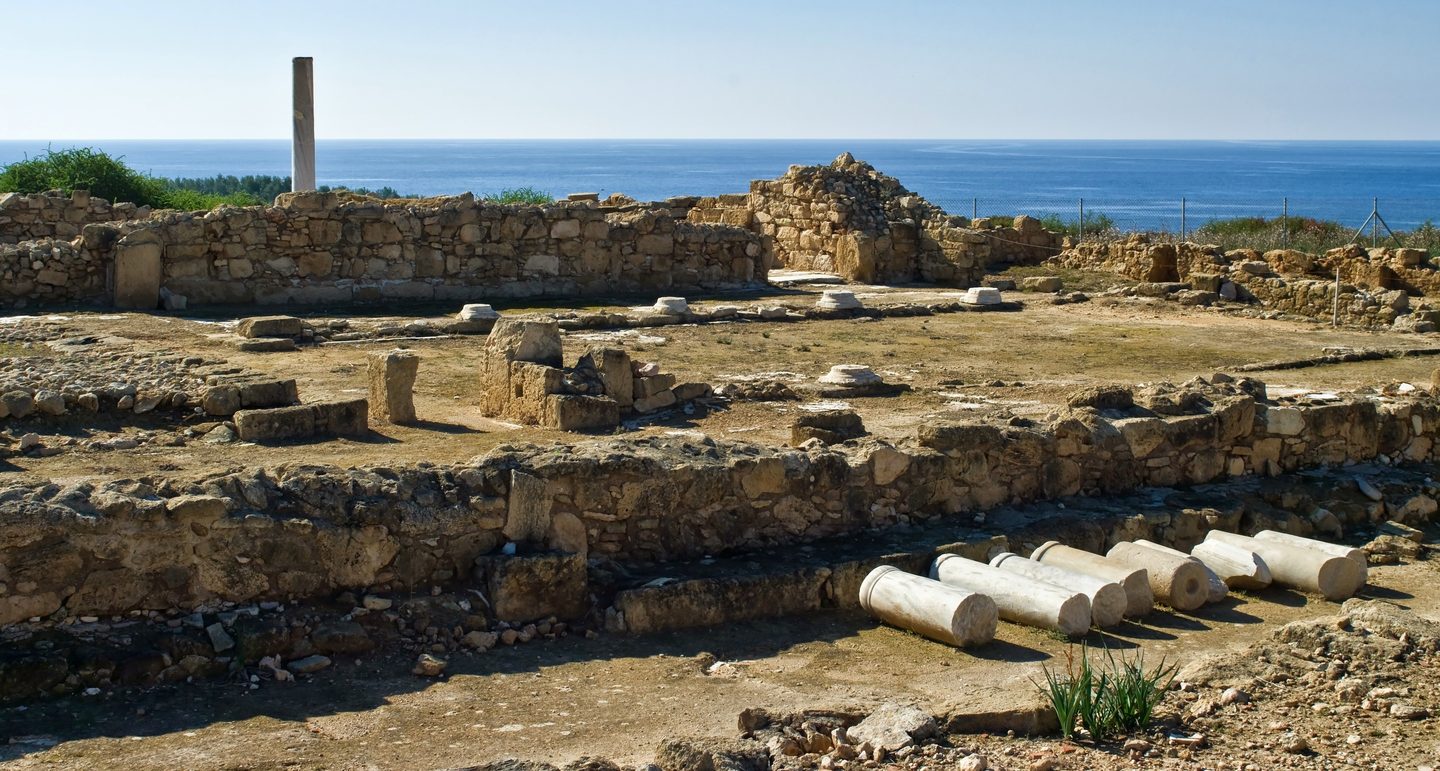 Excavated stone foundations and fallen columns on the Agios Georgios headland above a deep blue sea