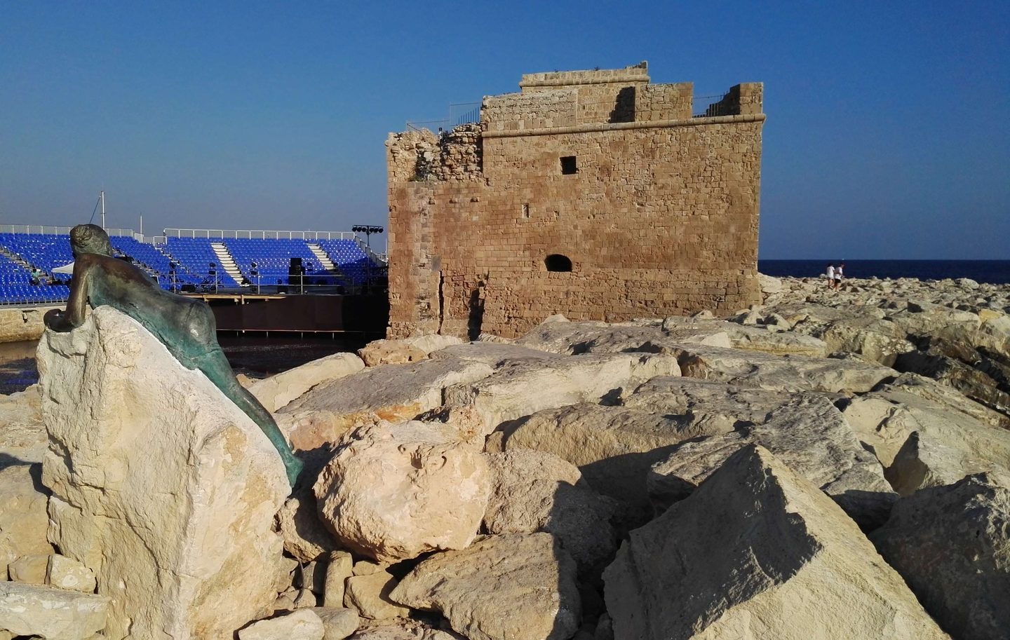 Paphos castle in evening light on the harbour mole, bronze sculpture on the rocks below
