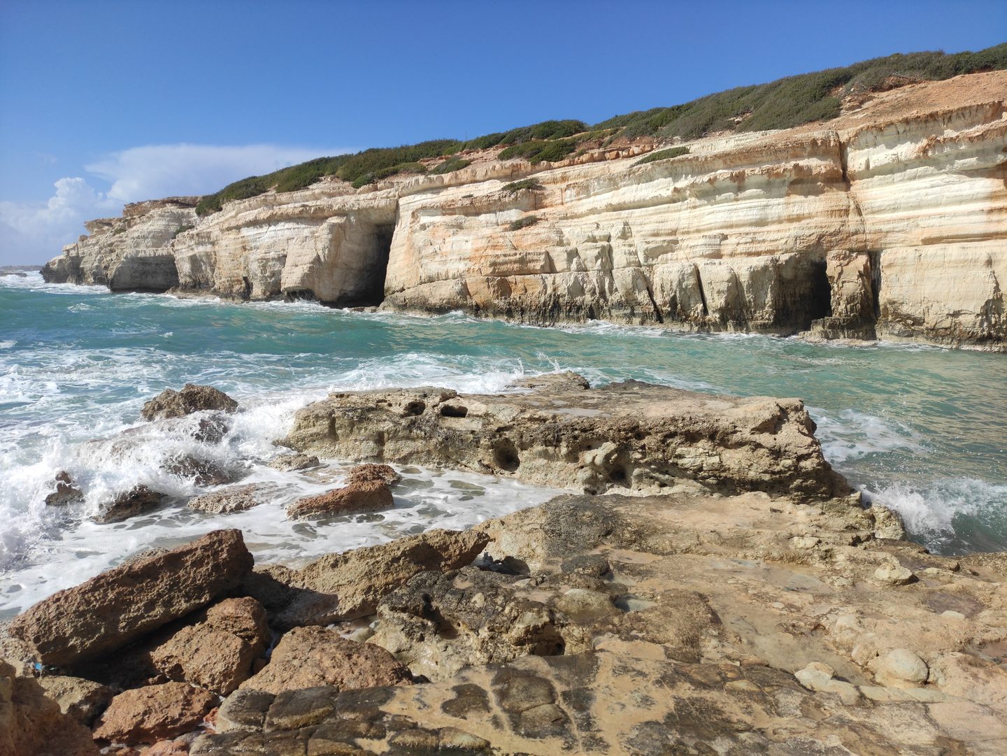 Layered white limestone cliffs undercut by caves above turquoise water at the Peyia sea caves