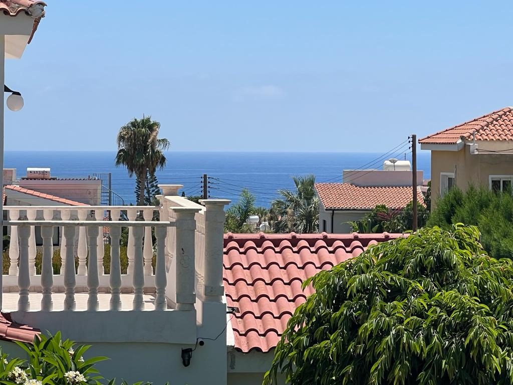 Open sea horizon beyond a white balustrade, terracotta rooftops and a lone palm