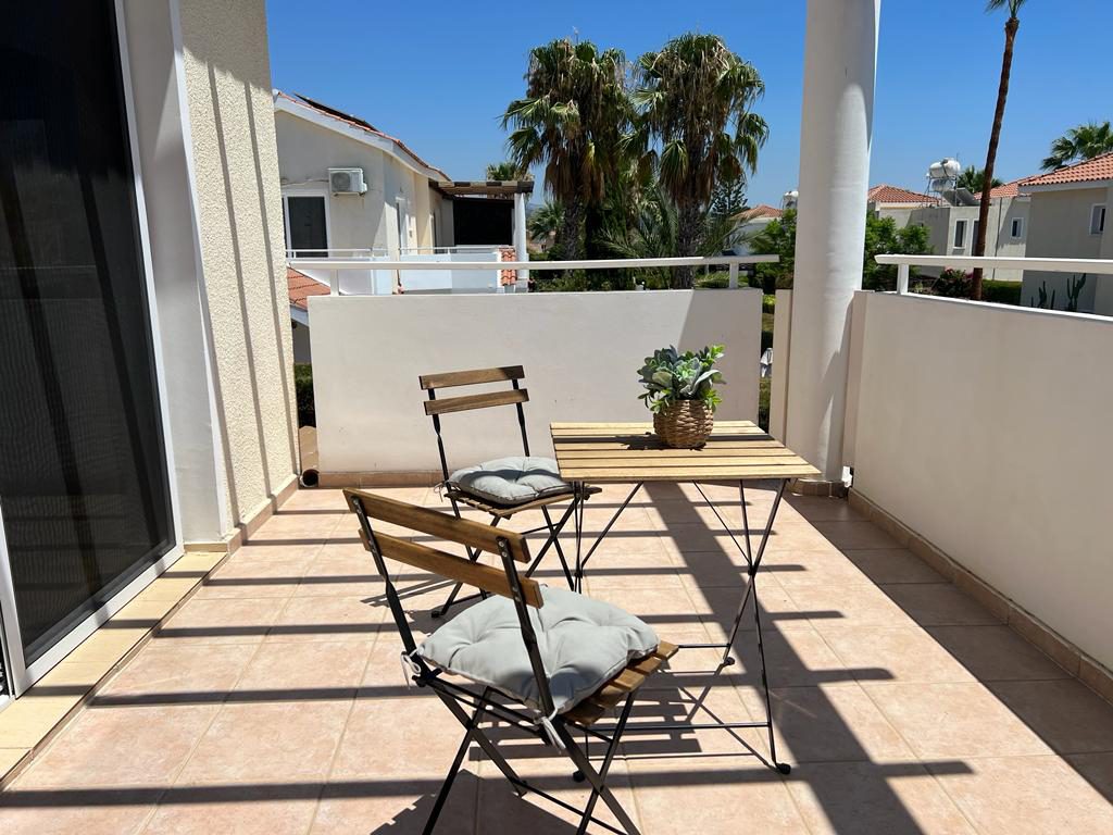 Sunny tiled balcony with a bistro table and chairs overlooking neighbouring palms