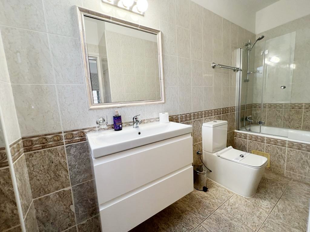 Tiled family bathroom with wall-hung vanity, mirrored light bar and bath with shower screen