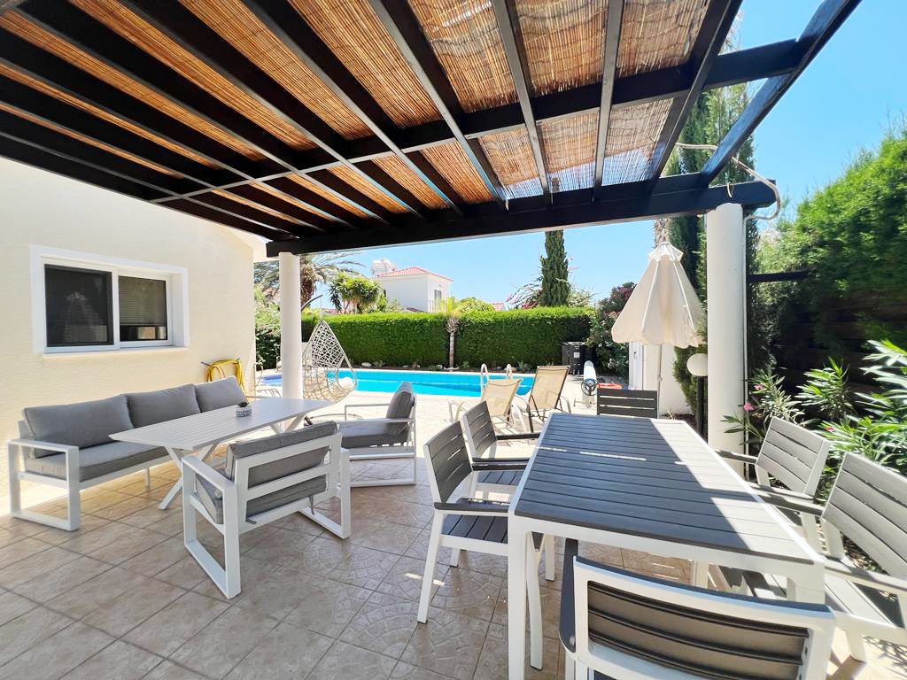 Shaded terrace under a bamboo pergola with sofas, dining table and the pool beyond