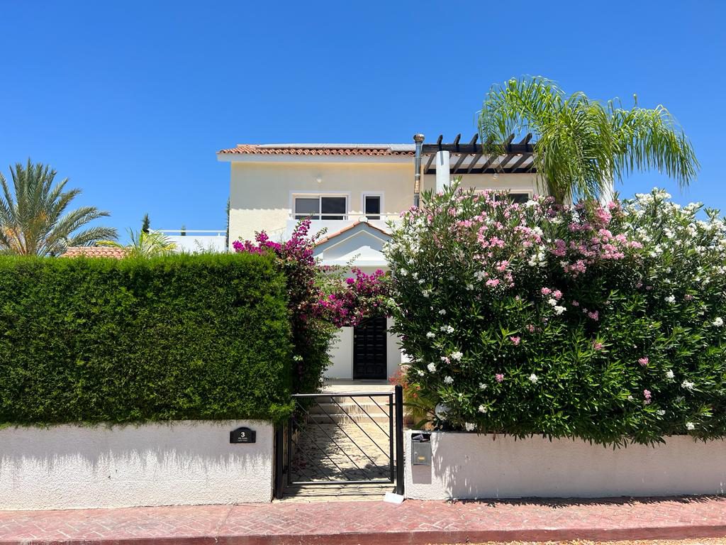 The villa seen from the street, its white walls set behind a clipped hedge