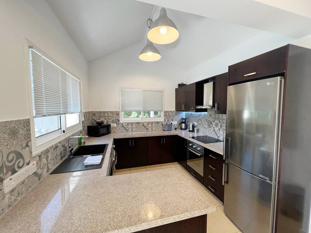 Well-equipped kitchen with dark wood units, granite worktops, ceramic hob and tall fridge freezer