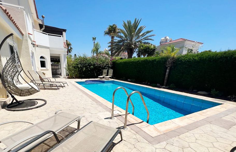 Poolside loungers and a hanging egg chair on the paved terrace beside the villa