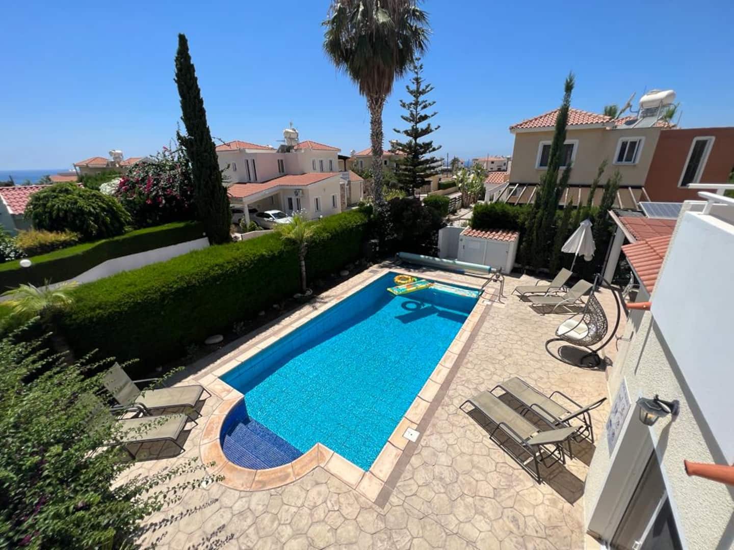 Pool and paved terrace seen from the balcony, with loungers, hanging chair and hedged garden