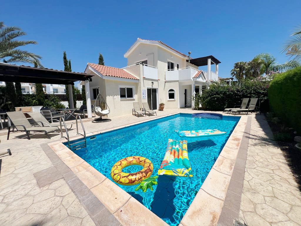 Sunlit swimming pool with inflatable floats, sun loungers and the cream villa behind