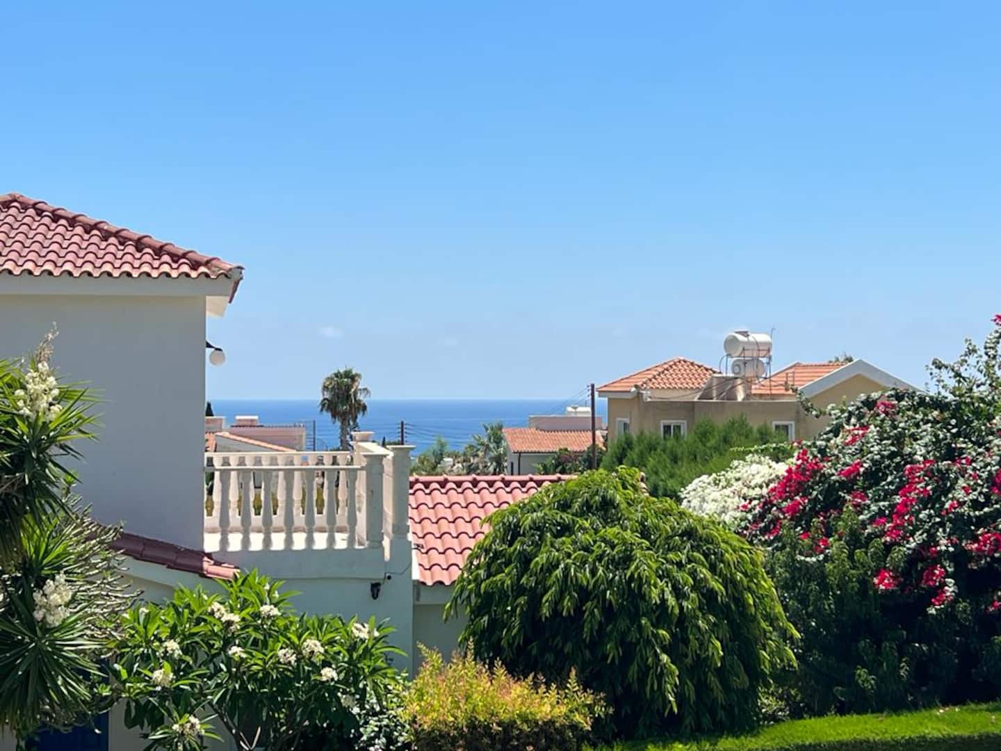 Sea glimpsed over tiled rooftops from the garden, framed by bougainvillea and oleander blossom