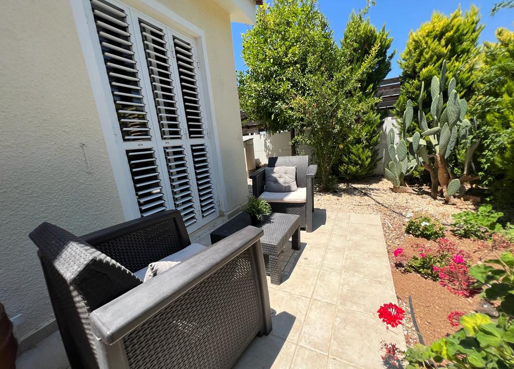 Rattan seating on a side terrace beside prickly pear cactus and flowering geraniums