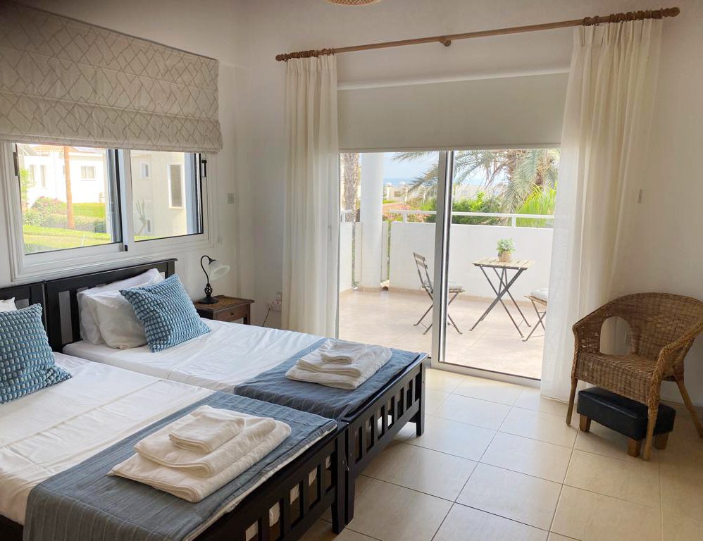 Twin bedroom opening onto a balcony with palm trees and the sea beyond