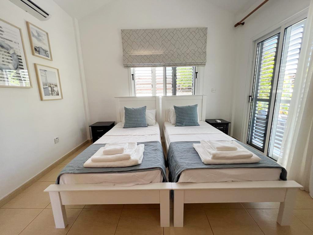 Twin bedroom with white bed frames, framed prints and shuttered balcony doors