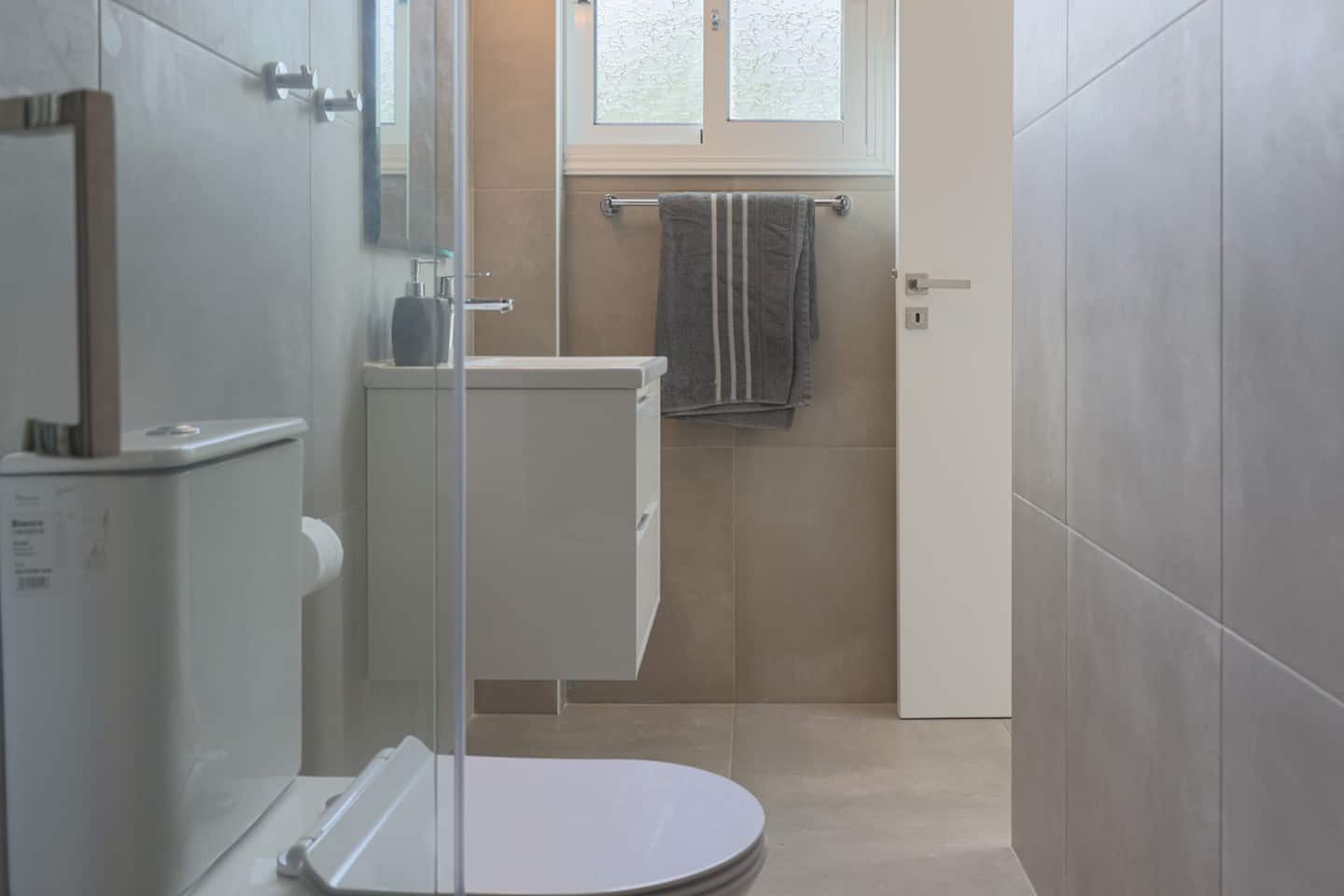 Grey-tiled bathroom with corner shower cubicle, wall-hung basin and heated towel rail