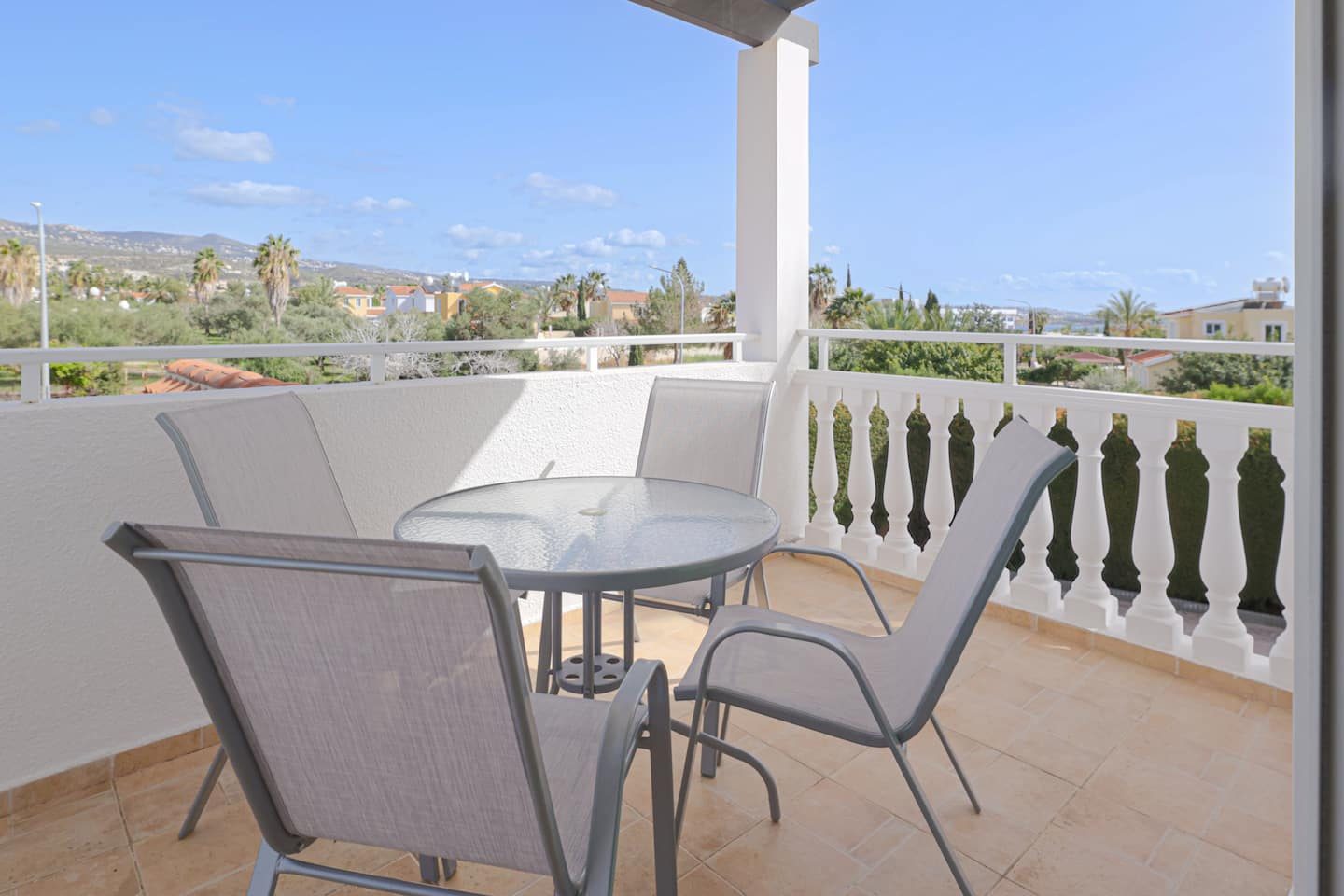 Private bedroom balcony with a glass bistro table and chairs facing the hills