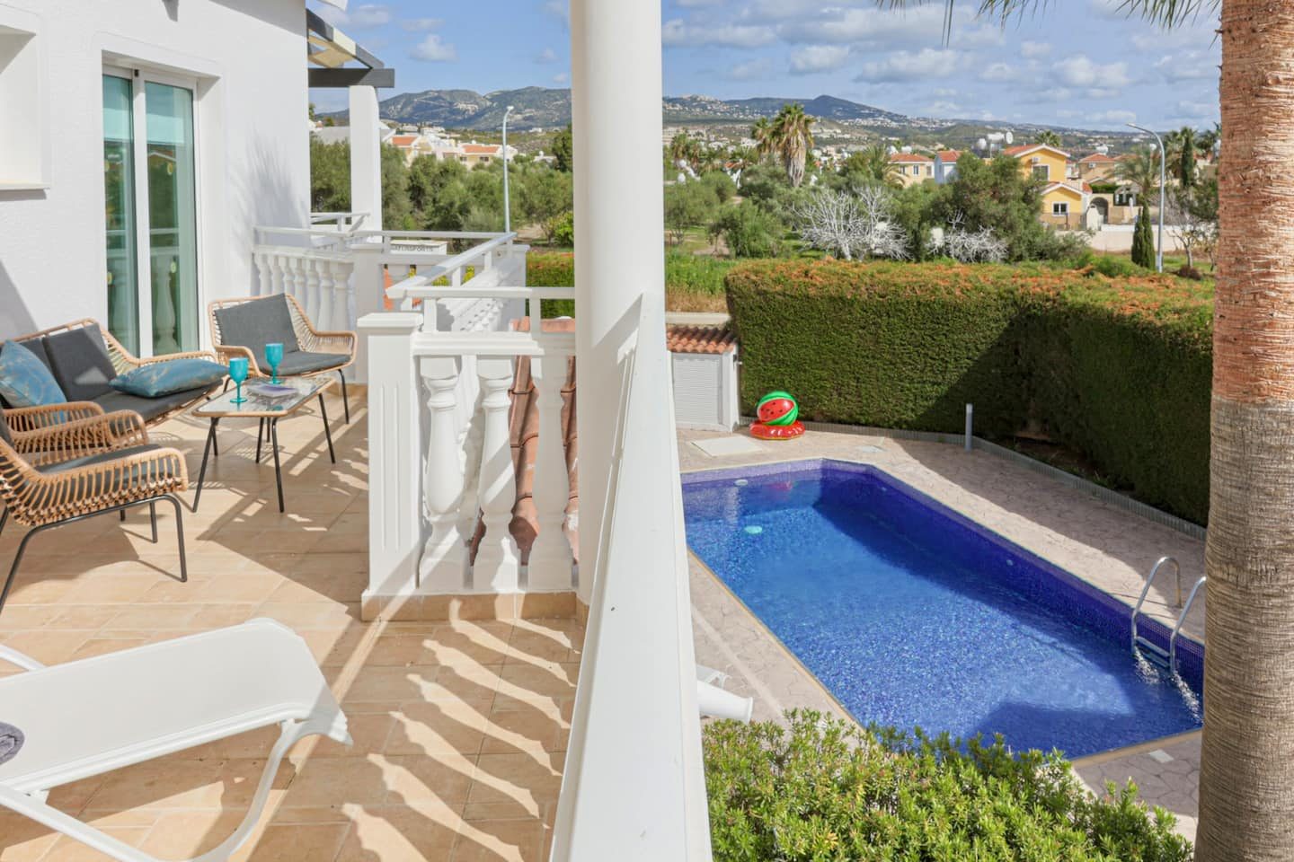Shaded terrace with rattan seating looking down over the pool to the Peyia hills