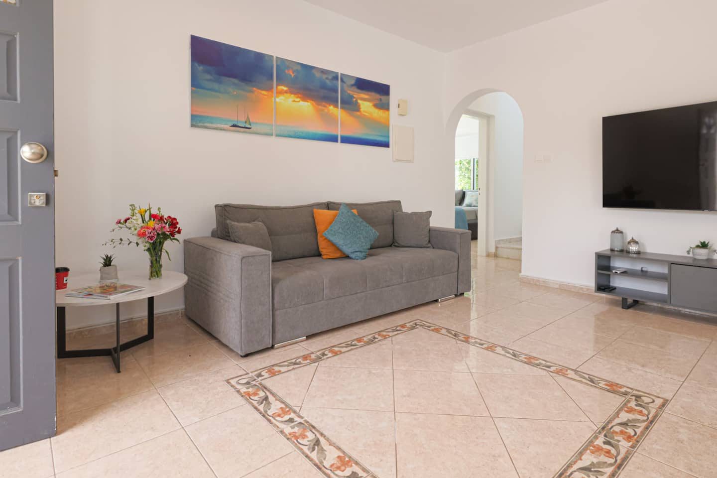 Sofa and television by the front door, with seascape triptych above