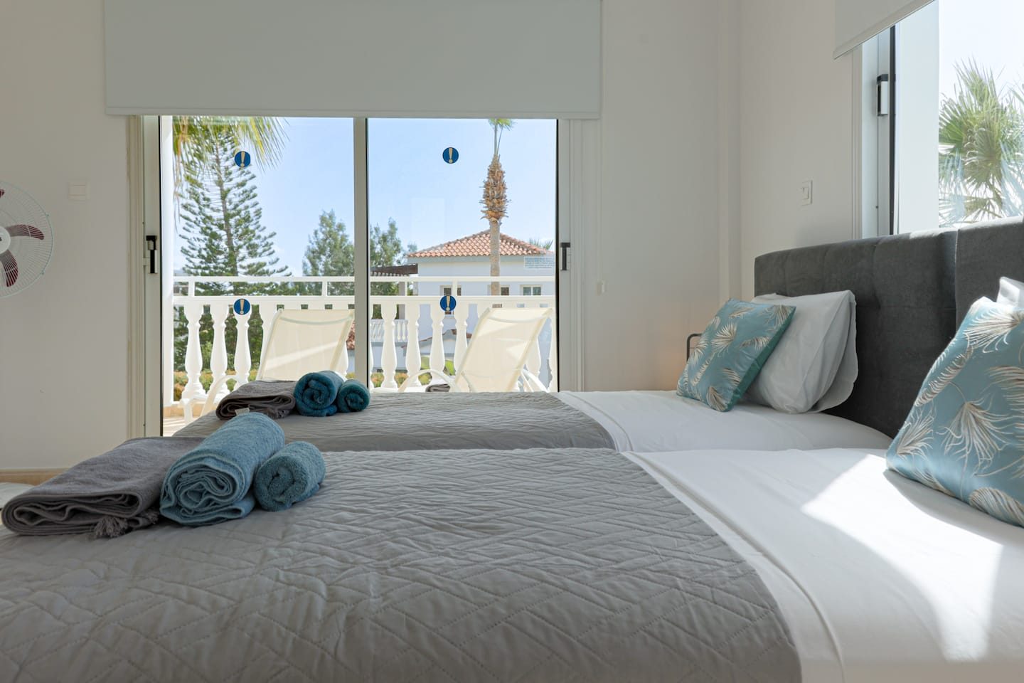 Twin beds beside balcony doors opening to palm trees and a strip of sea